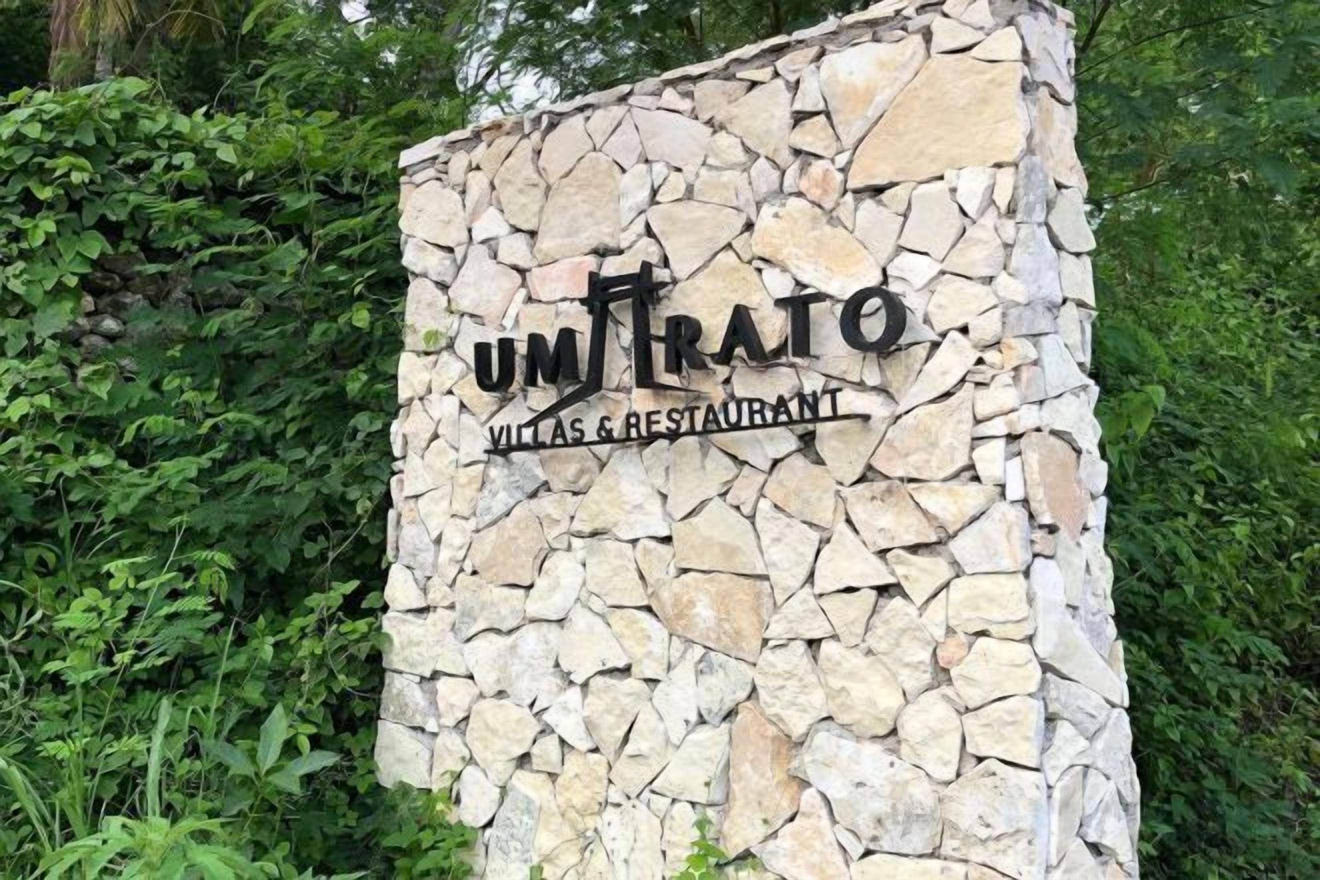 A stone wall with the text 'UM TRATO VILLAS & RESTAURANT' indicating a hotel and restaurant establishment.