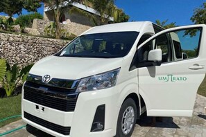 A white vehicle with 'UMRATO' branding, parked outdoors with a stone wall and greenery in the background. - Umarato Villa Sumba (Wanokaka)