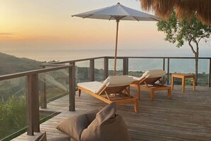 Una terraza de madera con una silla de salón y una sombrilla, con vista a una extensión de agua.