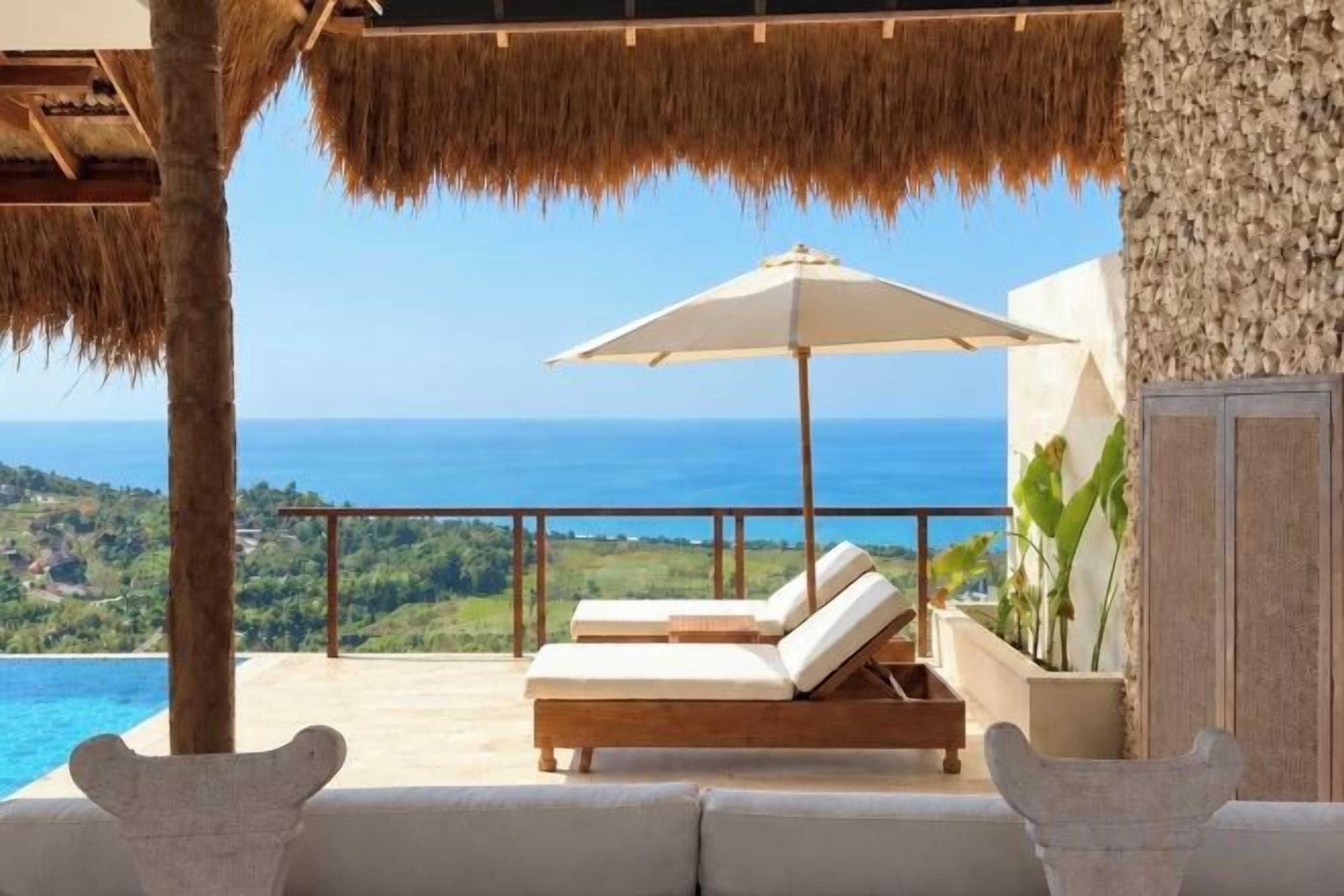 A balcony with a view of the sea, a lounge chair, and a large umbrella.