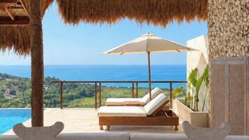 A balcony with a view of the sea, a lounge chair, and a large umbrella.