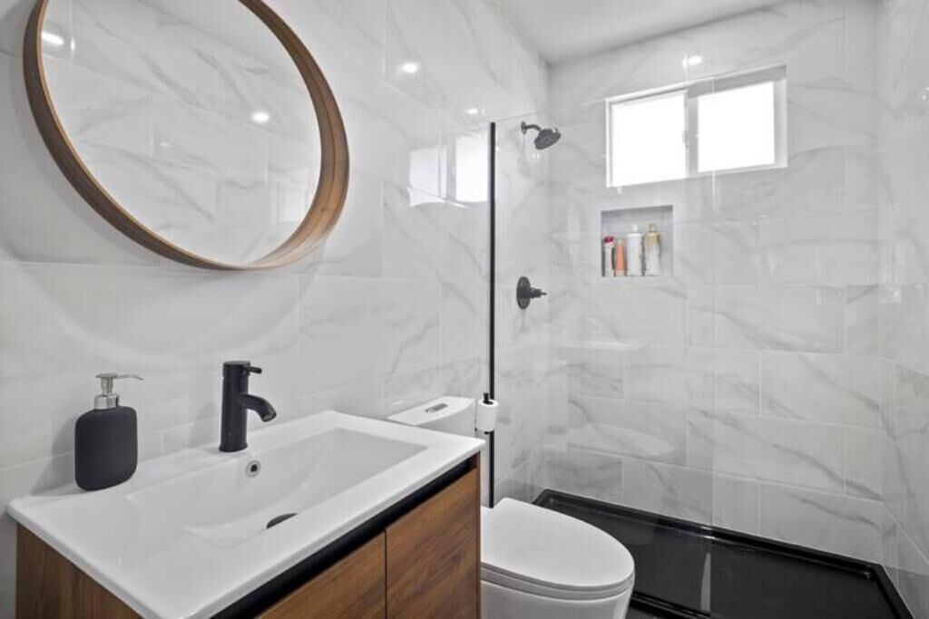 A modern bathroom with a white sink, black faucet, and a round mirror.