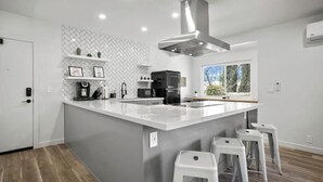 Een moderne keuken met een groot eiland, witte barstoelen en een backsplash met een herringbone-patroon.