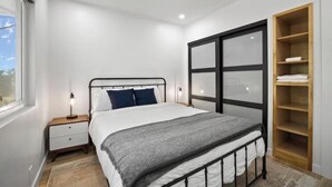 Een slaapkamer met een bed, nachtkastjes, een houten garderobe en een raam.