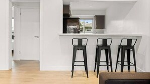 Une cuisine moderne avec des murs blancs, un plancher en bois et trois tabourets de bar noirs.