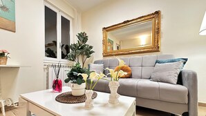 Een woonkamer met een grijze bank, een witte salontafel, een grote spiegel en een potplant.