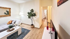 Een moderne woonkamer met een bank, salontafel en een potplant. Een hal leidt naar een badkamer.