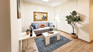Een woonkamer met een grijze bank, een witte salontafel, een blauw vloerkleed, een kamerplant en een vloerlamp.