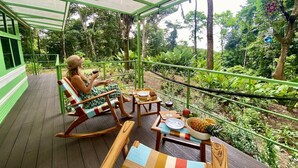 A covered outdoor seating area with wooden furniture and a dining table, surrounded by lush greenery. - Jungle Bus, 5 min drive PlayaLinda, 15 x Dominical, Wifi Starlink (Savegre de Aguirre)