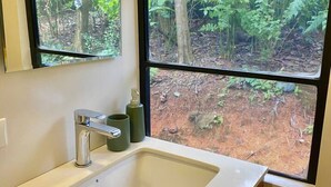 A bathroom with a sink, mirror, and window with a forest view. - Jungle Bus, 5 min drive PlayaLinda, 15 x Dominical, Wifi Starlink (Savegre de Aguirre)