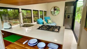 A modern kitchen with a built-in stove, sink, and a window overlooking greenery. - Jungle Bus, 5 min drive PlayaLinda, 15 x Dominical, Wifi Starlink (Savegre de Aguirre)