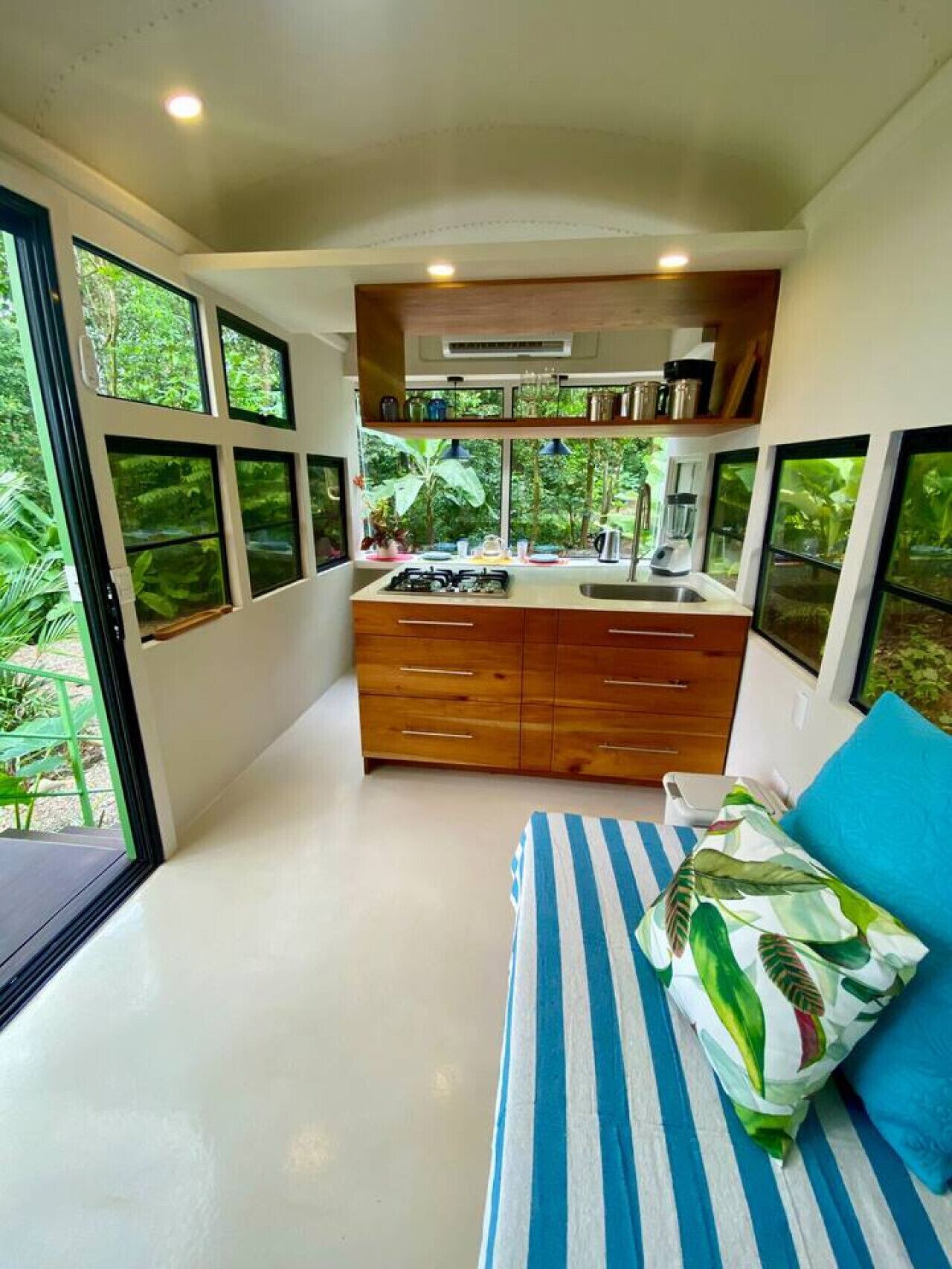 A compact bedroom with a bed, a small kitchenette, and large windows.