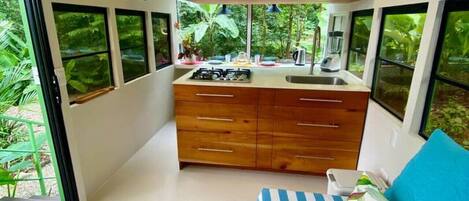 A compact bedroom with a bed, a small kitchenette, and large windows.