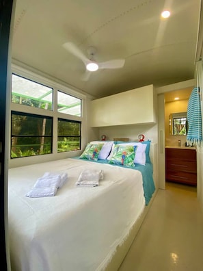 Ein Schlafzimmer mit einem Bett, einem Deckenventilator und einem Fenster mit Blick auf Grünflächen.