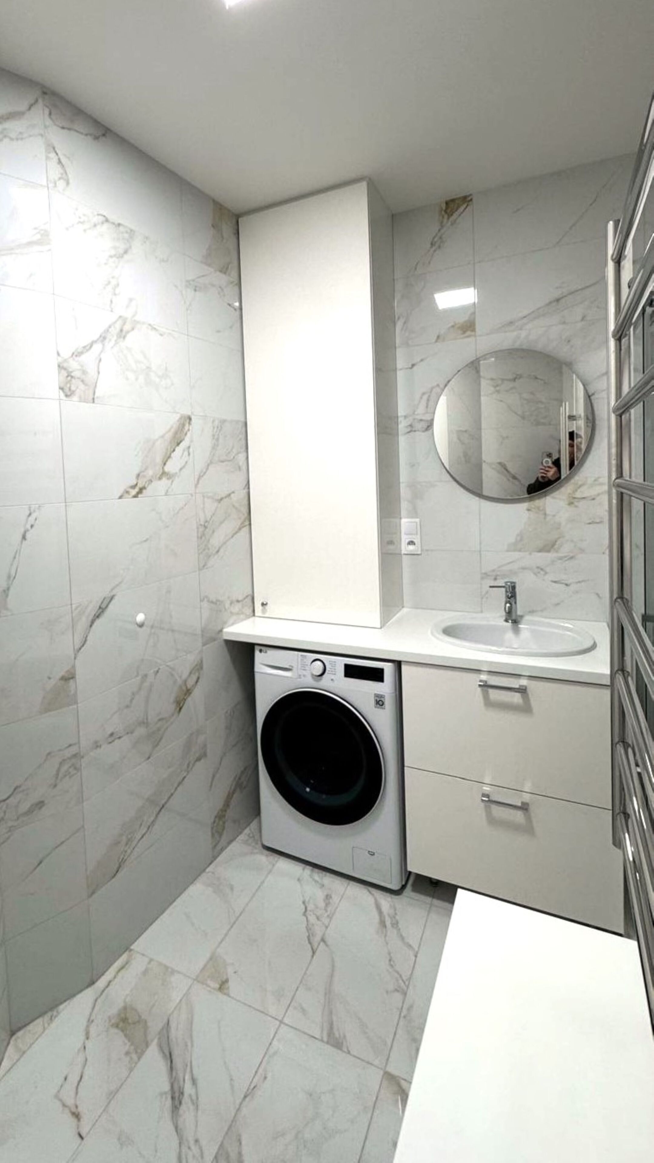 A compact bathroom with a washing machine, a sink, and a mirror.