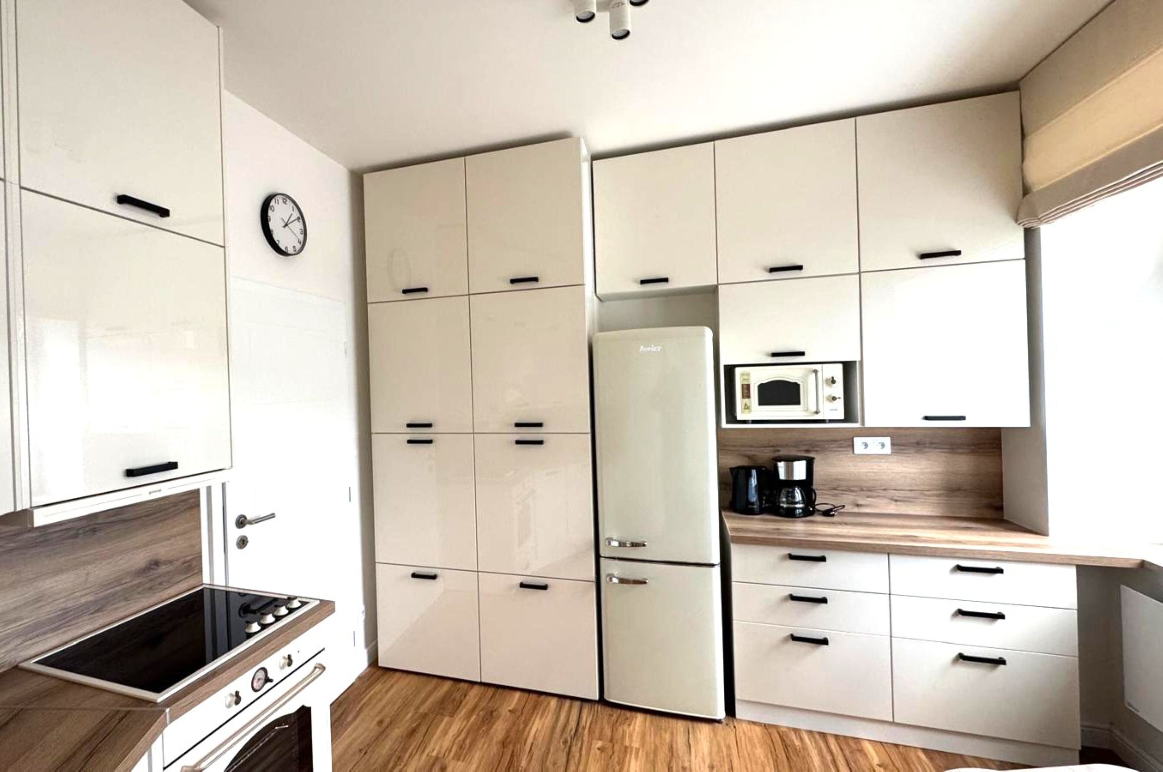 Een compacte keuken met witte kastjes, een magnetron, een koelkast en een fornuis.