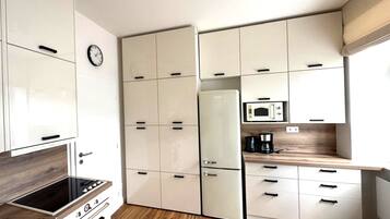 Een compacte keuken met witte kastjes, een magnetron, een koelkast en een fornuis.