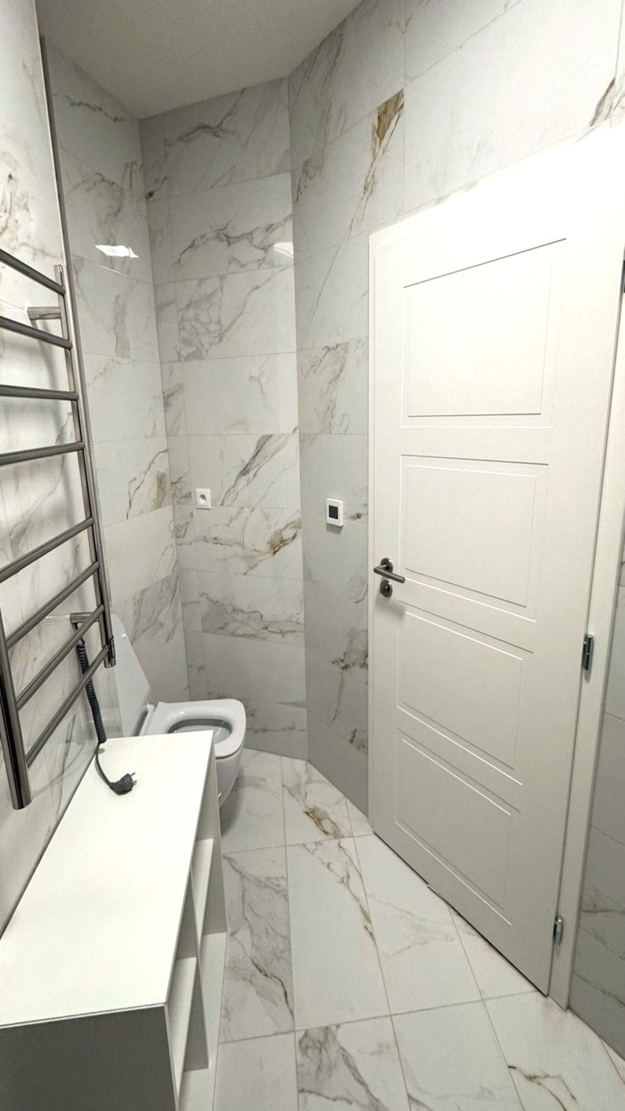 A bathroom with a marble floor, a toilet, a white door, and a towel rack.