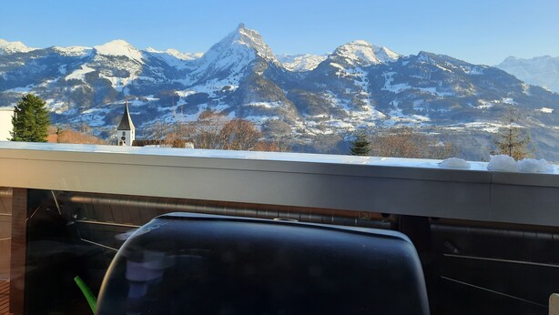 A view of snow-covered mountains from inside a vehicle, with a church visible in the foreground. - Epic view and sun sets from spacious 4 bedroom apartment. Large families +groups (Amden)