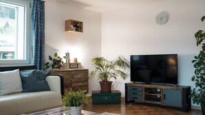 A living room with a sofa, a television, a wooden cabinet, and a potted plant. - Epic view and sun sets from spacious 4 bedroom apartment. Large families +groups (Amden)