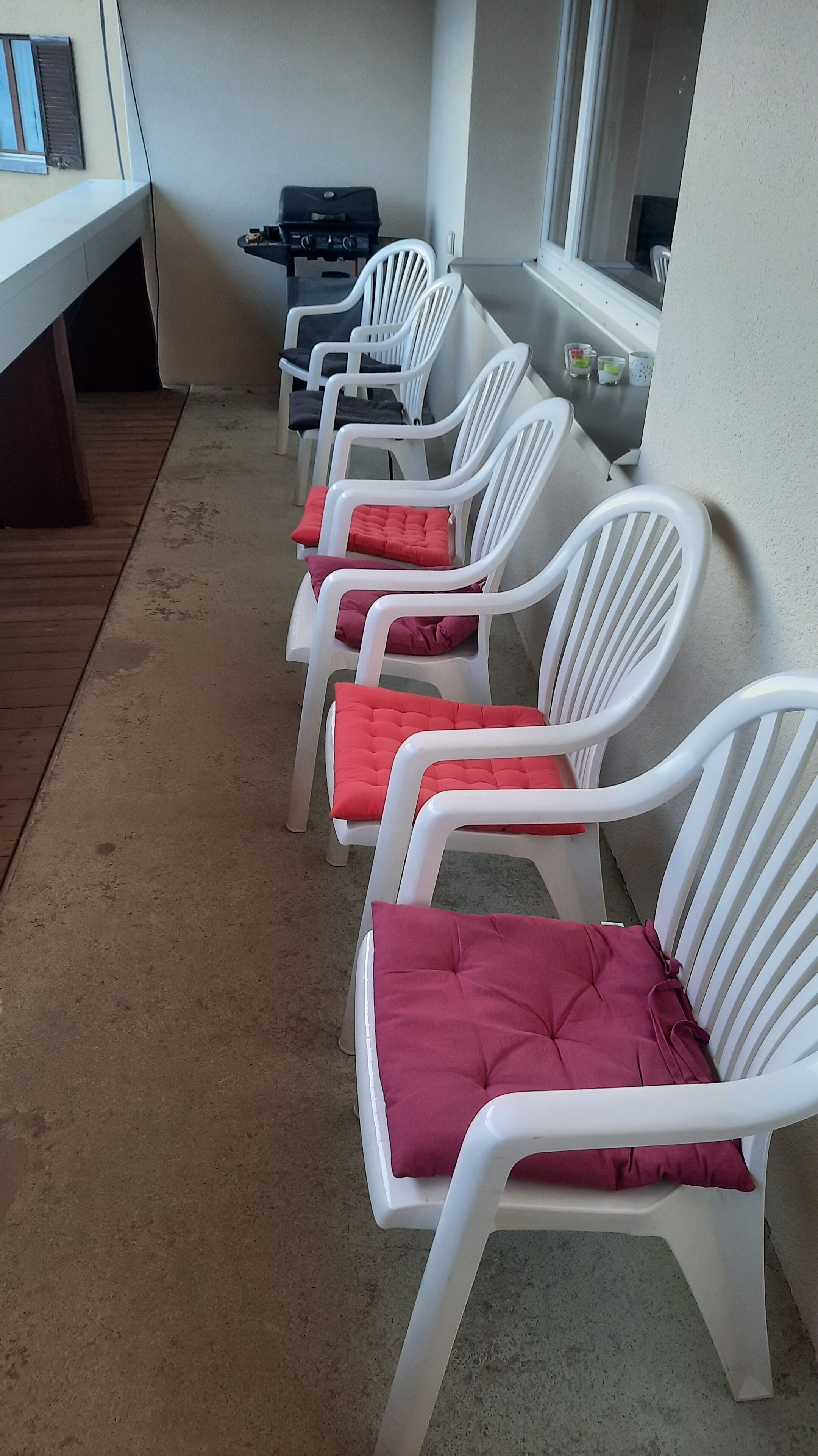 Une rangée de chaises en plastique blanc, dotées de coussins rouges, est disposée en ligne sur un sol en béton.