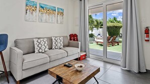 Un salón moderno con un sofá gris, una mesa de centro de madera y vistas a un jardín a través de puertas correderas grandes.