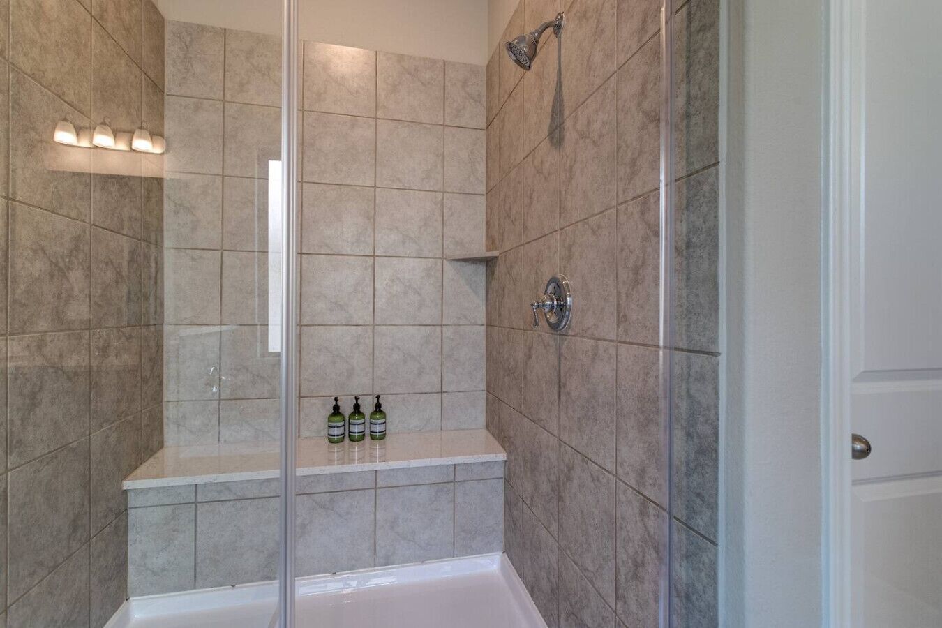 A modern bathroom with a glass shower enclosure, a bathtub, and a shelf with toiletries.
