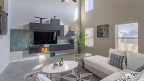 Un salon spacieux doté d’une cheminée, d’un ventilateur de plafond et d’une grande fenêtre laissant entrer la lumière naturelle.