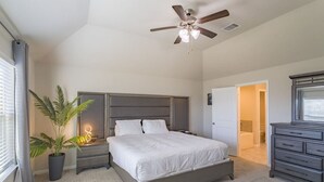 Une chambre à coucher comprenant un lit, des tables de chevet, un ventilateur de plafond, une plante en pot et une commode.