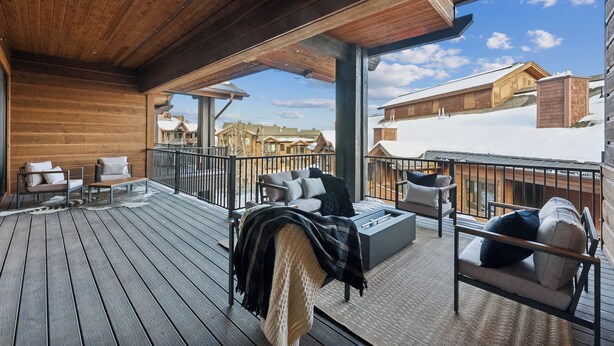 Een houten terras met buitenmeubilair en uitzicht op besneeuwde gebouwen.