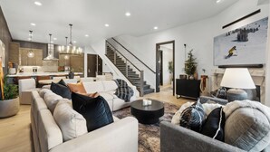 Een moderne woonkamer met een bank, fauteuils en een salontafel. Er is een trap die naar een ander niveau leidt.
