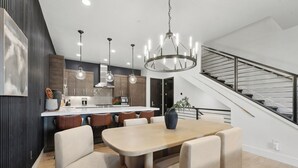 Een moderne keuken met een centraal eiland, hanglampen en een trap met een metalen leuning.