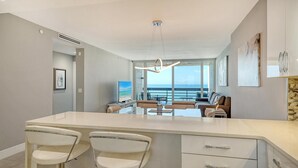 A modern kitchen with a large island, bar stools, and a view of the ocean.
