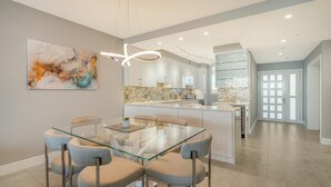A modern kitchen with white cabinets, a glass island, and a contemporary pendant light.