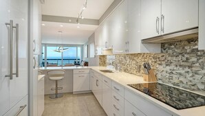 A modern kitchen with white cabinets, a stone backsplash, and a view of the ocean.