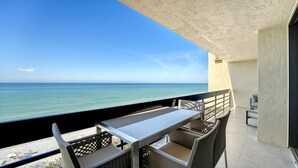 A balcony with a view of the ocean, a table, and two chairs.
