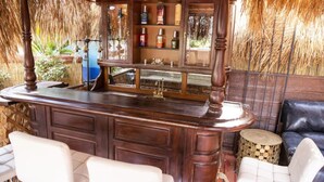 Een bar met een houten toonbank, flessenkasten en een zithoek met witte stoelen.