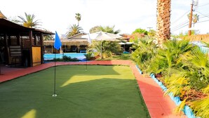 Een golfbaan met een putting green, een zwembad en tropische beplanting.