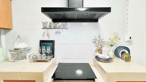 Een keuken met een zwarte afzuigkap, witte tegels, een inbouwoven en diverse keukengadgets op het aanrecht.