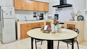 Een kleine keuken met houten kastjes, een witte koelkast, een ronde eettafel met stoelen en een zwarte afzuigkap.