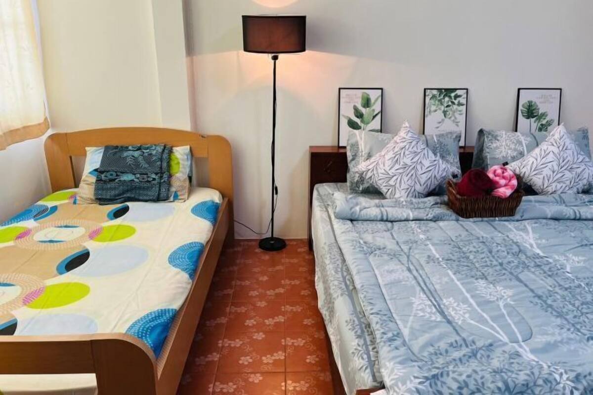 A bedroom with two beds, a floor lamp, and framed botanical prints on the wall.