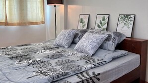 Een slaapkamer met een bed, een nachtkastje, een lamp en ingelijste botanische prints aan de muur.