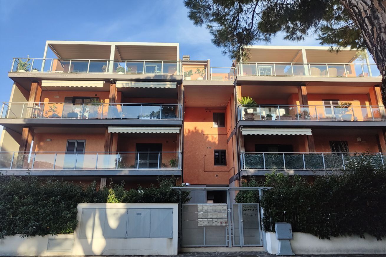 A multi-story residential building with balconies, a gated entrance, and potted plants.