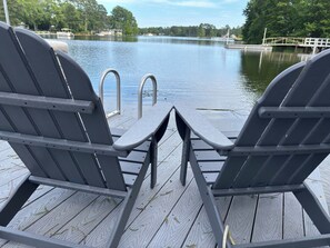 Two Adirondack chairs facing a wooden deck over a body of water with a dock and a small bridge in the background. - Private dock, swim, fish, kayak, play games in the large, modern barn (Prosperity)