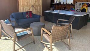 Una habitación acogedora con un sofá azul, sillones de mimbre, una pequeña mesa redonda y una mesa de ping pong.