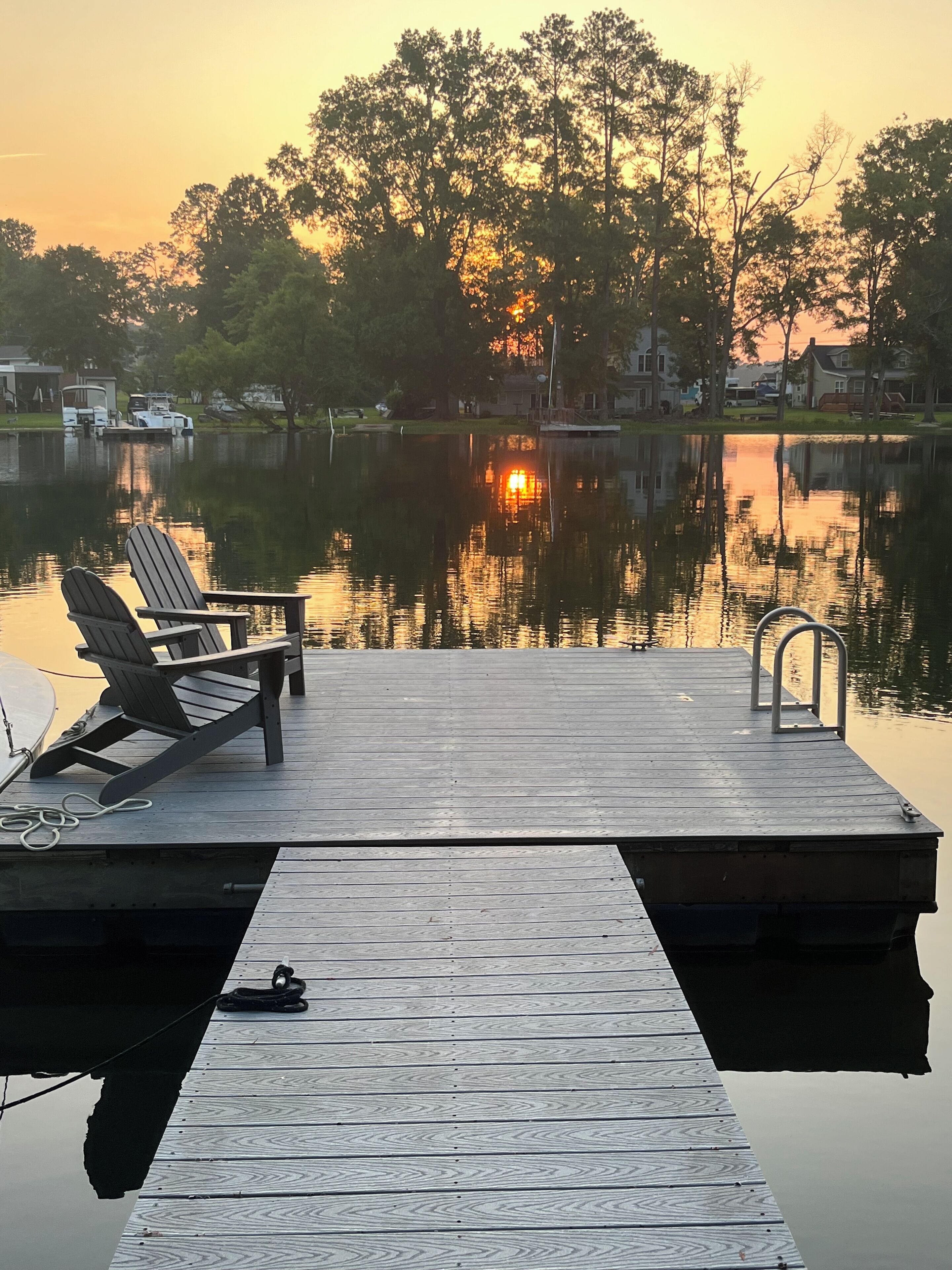 A wooden dock with two Adirondack chairs and a boat.