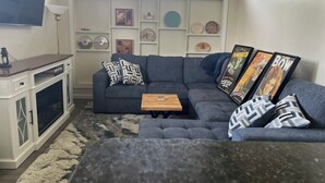 Una sala de estar con un sofá modular, una mesa de centro, un aparador con puertas de vidrio y adornos en la pared.