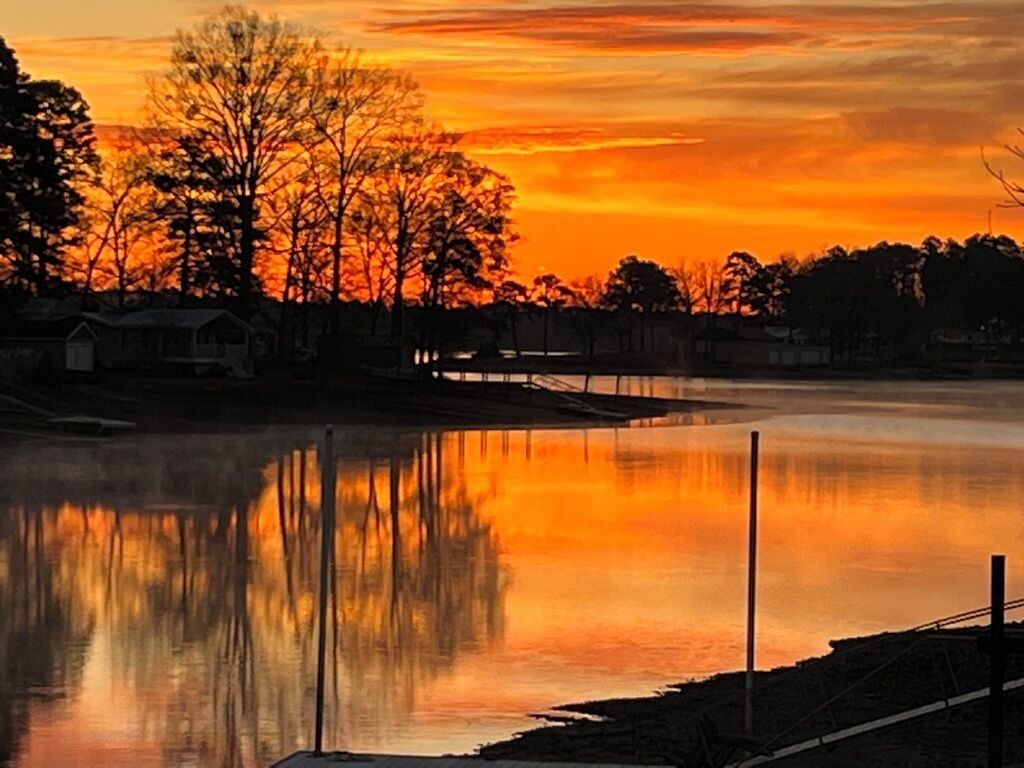 Una escena serena al costat d'un llac, amb un reflex del capvespre, aigua tranquil·la i un moll.