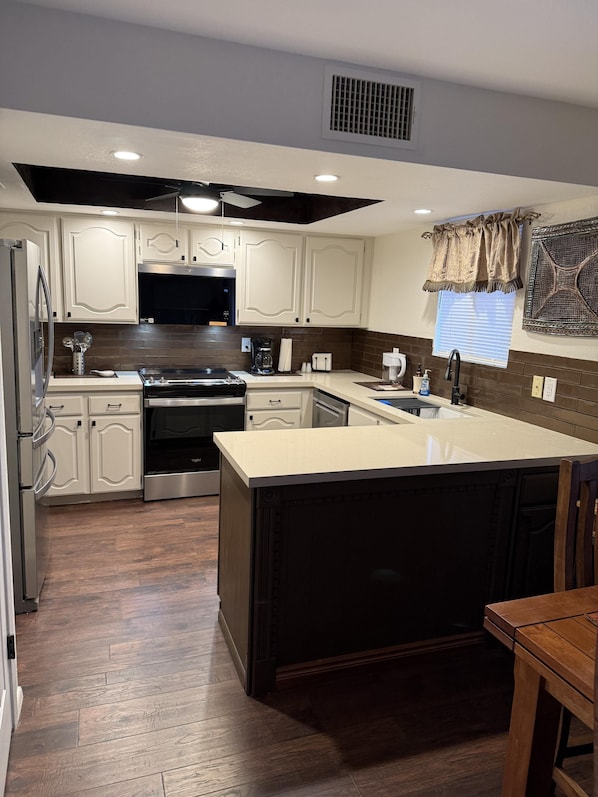 A modern kitchen with white cabinetry, a central island, and a dark wood floor. - CASA RANCHERO: Cowboy up, golf course view. (Phoenix, Arizona)