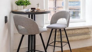 A corner room with two chairs, a small table, a potted plant, and a window with a view of buildings. - Nexus Rentals Tallinn (Tallinn)